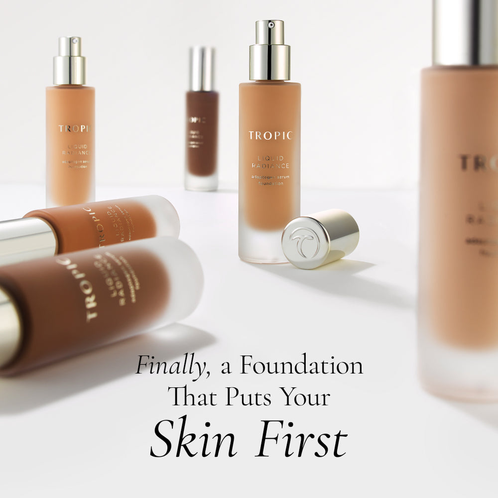 Several Tropic Fluid Radiance liquid foundation bottles and tubes arranged on a clean white studio background, with one bottle open and its cap beside it. Large text at the bottom reads, 'Finally, a Foundation That Puts Your Skin First.